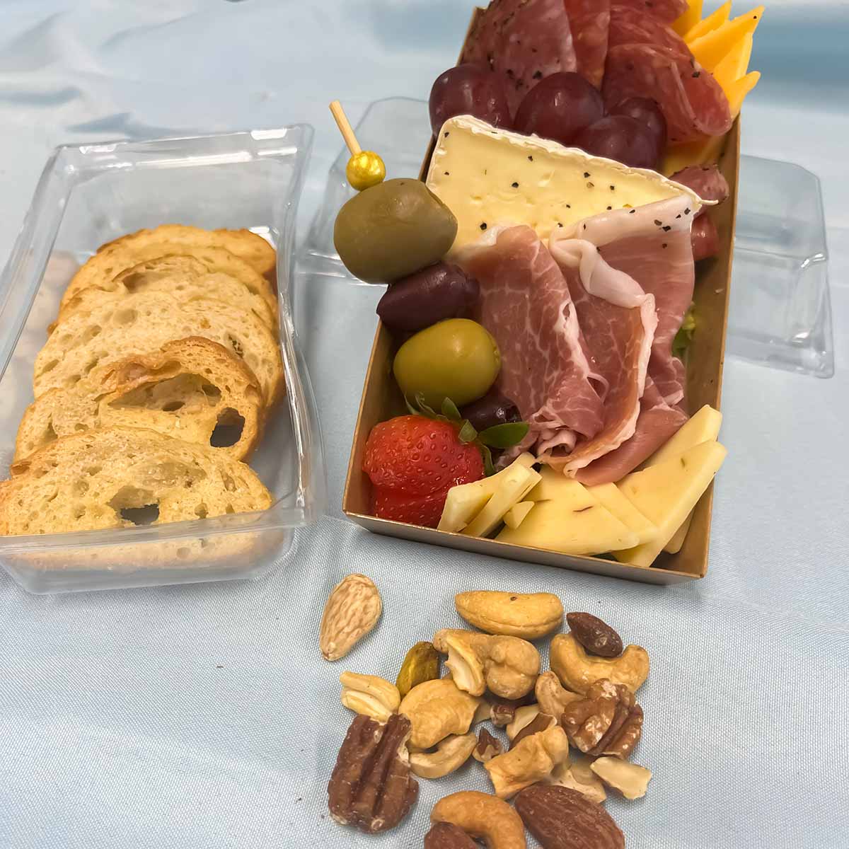 individual charcuterie with three meats, three cheeses, grapes, strawberry,green and kalamata olives and garlic toast and nuts
